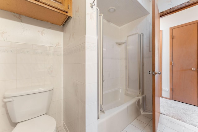 bathroom with tile patterned flooring, tiled shower / bath combo, tile walls, and toilet