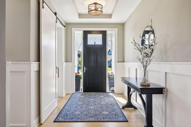 entrance foyer featuring a tray ceiling, a barn door, and light wood-type flooring