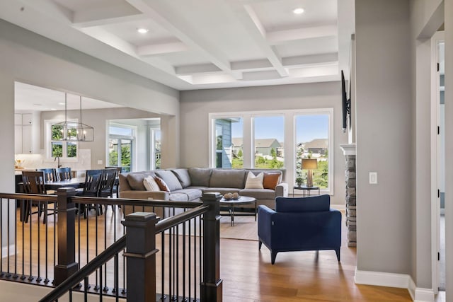 living room featuring light wood-type flooring, coffered ceiling, beamed ceiling, and an inviting chandelier