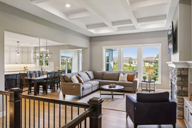 living room featuring a fireplace, coffered ceiling, light hardwood / wood-style floors, and beamed ceiling