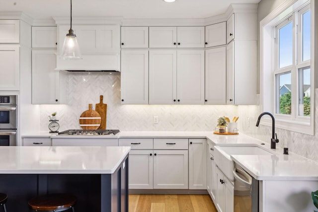 kitchen with hanging light fixtures, appliances with stainless steel finishes, sink, tasteful backsplash, and white cabinetry