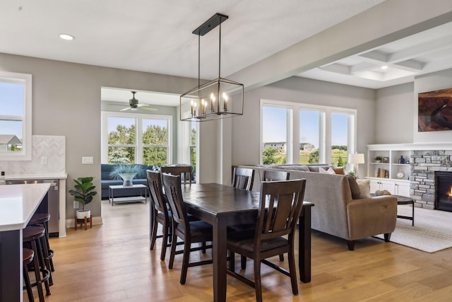 dining room with light hardwood / wood-style floors, a wealth of natural light, coffered ceiling, and a fireplace