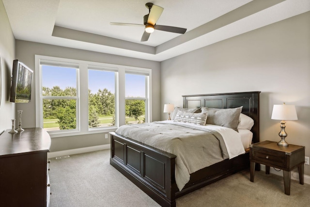 carpeted bedroom with ceiling fan and a raised ceiling