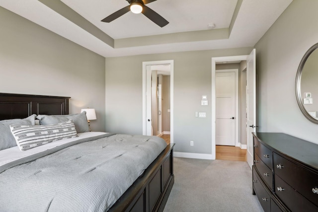 bedroom featuring light carpet, a tray ceiling, and ceiling fan