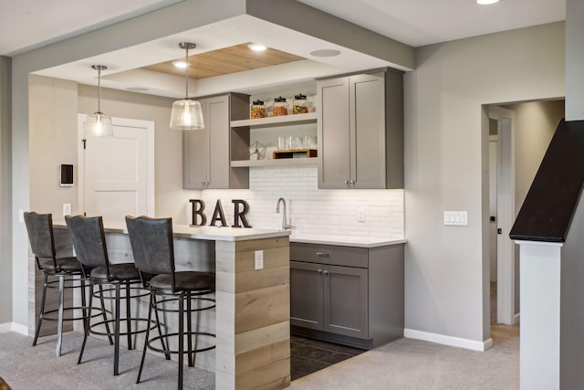 kitchen featuring pendant lighting, tasteful backsplash, gray cabinetry, dark colored carpet, and a kitchen bar