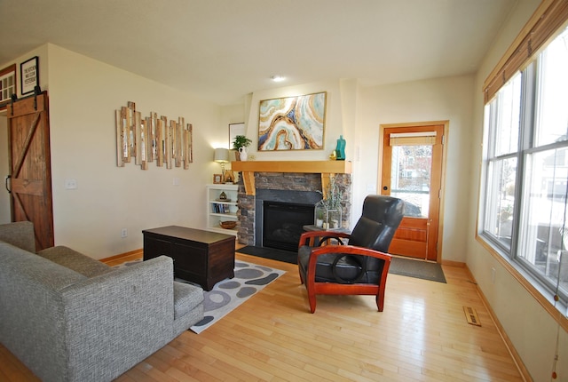 living room featuring a barn door, a stone fireplace, and light hardwood / wood-style floors