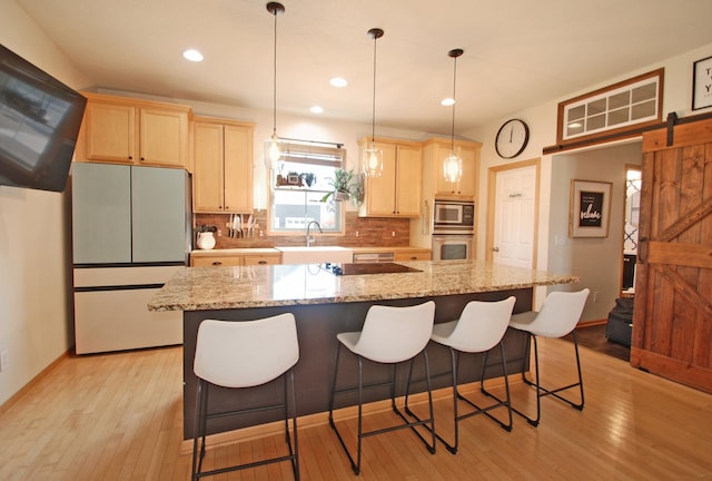 kitchen with appliances with stainless steel finishes, sink, a large island, light stone counters, and a barn door