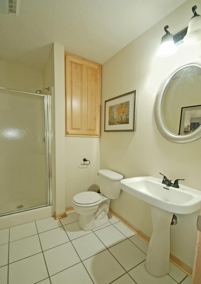 bathroom featuring tile patterned floors, a shower with door, toilet, and a textured ceiling