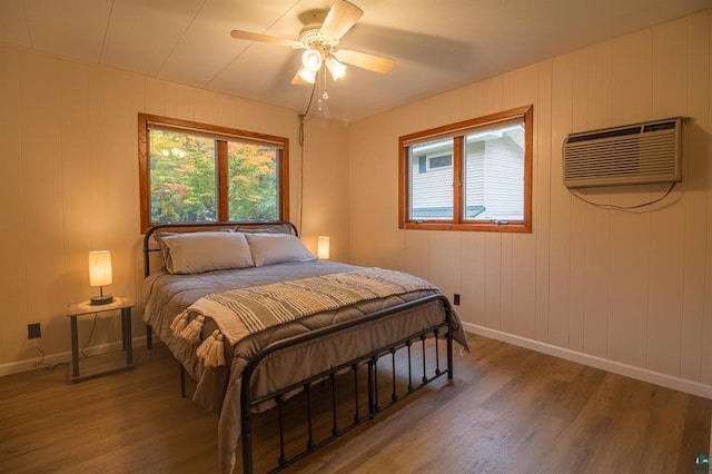 bedroom featuring ceiling fan, wood walls, wood-type flooring, and a wall unit AC