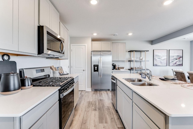 kitchen featuring appliances with stainless steel finishes, sink, white cabinets, light hardwood / wood-style flooring, and a center island with sink