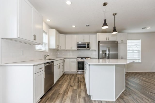 kitchen with stainless steel appliances, white cabinetry, a kitchen island, and decorative light fixtures