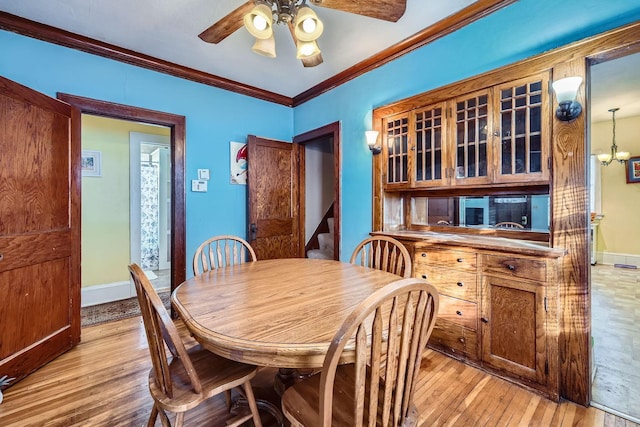 dining space with ceiling fan with notable chandelier, ornamental molding, and light hardwood / wood-style floors