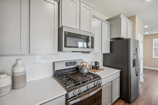 kitchen featuring appliances with stainless steel finishes, dark hardwood / wood-style flooring, gray cabinets, and backsplash