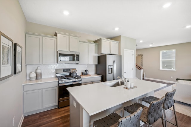 kitchen featuring sink, tasteful backsplash, dark hardwood / wood-style flooring, stainless steel appliances, and a kitchen island with sink