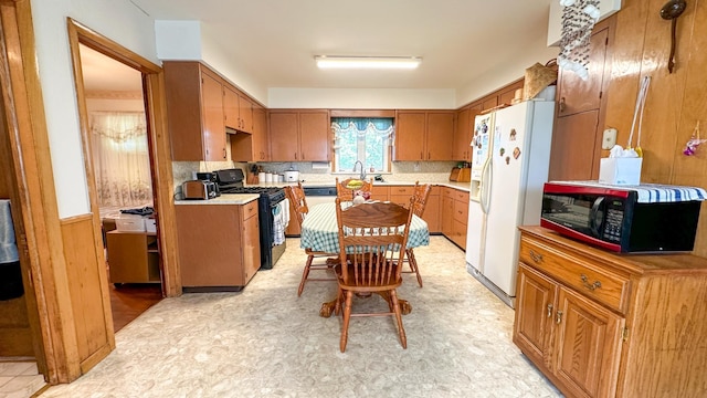 kitchen with sink, black gas stove, white refrigerator with ice dispenser, and wooden walls