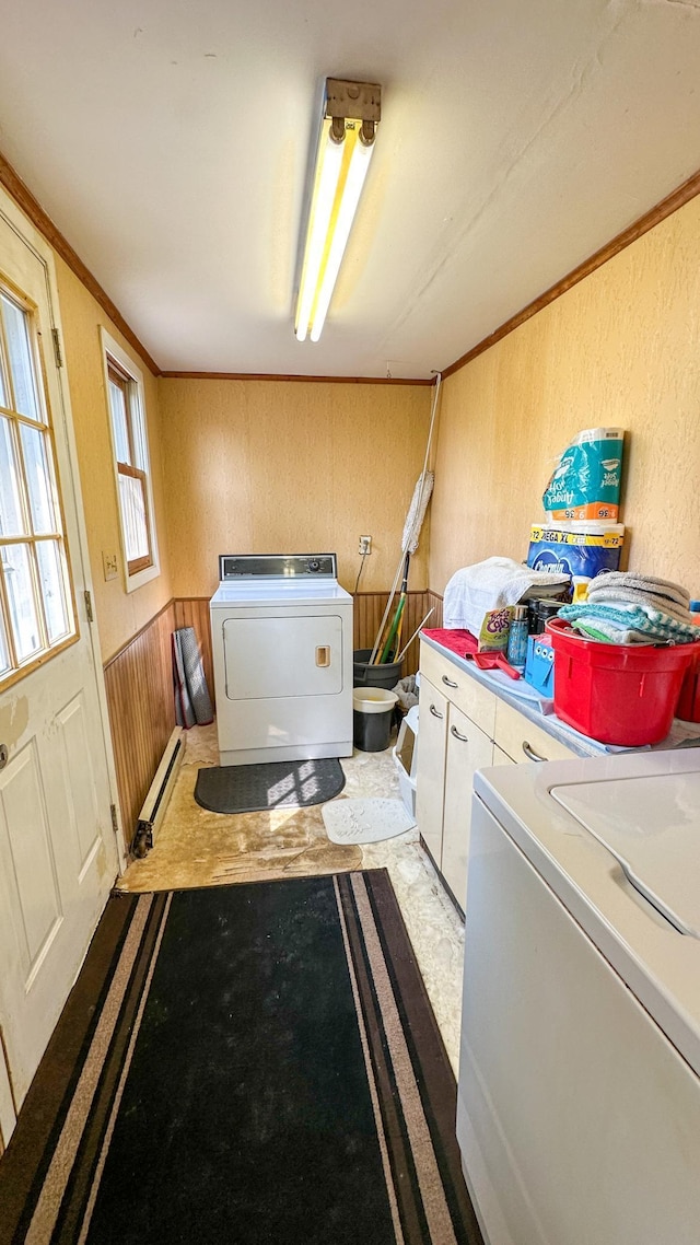 clothes washing area featuring wooden walls, baseboard heating, ornamental molding, washer and dryer, and cabinets