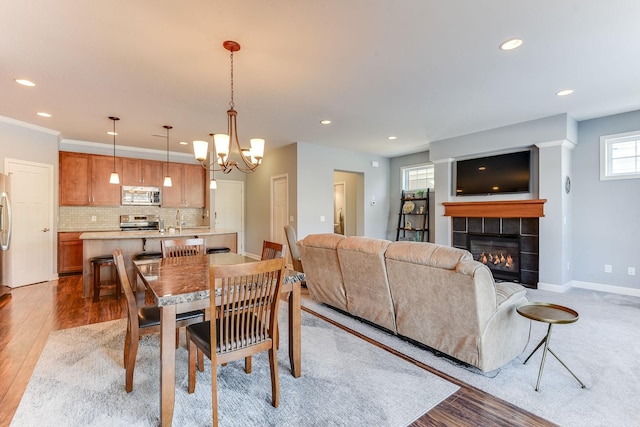 dining room featuring sink, a chandelier, a tile fireplace, and light hardwood / wood-style flooring