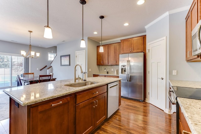 kitchen with stainless steel appliances, hanging light fixtures, sink, and a kitchen island with sink