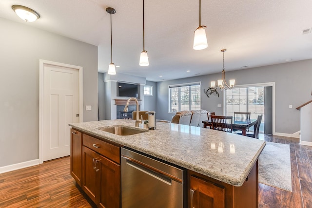 kitchen featuring sink, hanging light fixtures, a center island with sink, stainless steel dishwasher, and light stone countertops