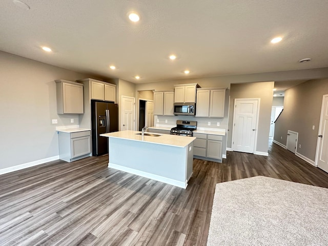 kitchen with gray cabinets, dark hardwood / wood-style floors, sink, stainless steel appliances, and a center island with sink