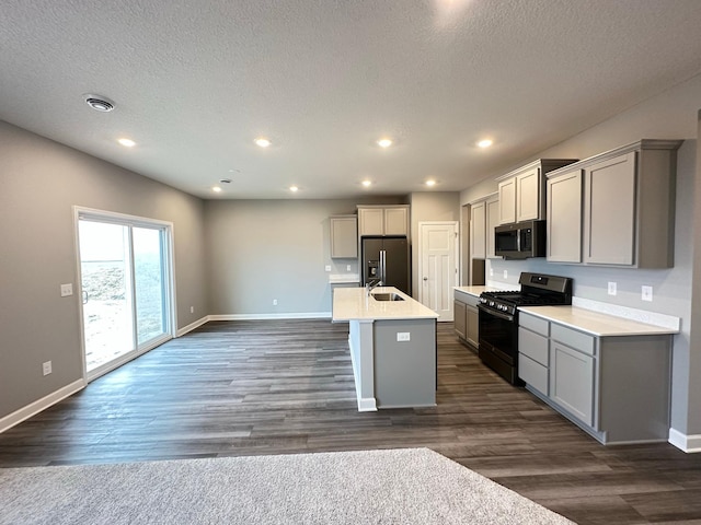 kitchen with gray cabinetry, a kitchen island with sink, stainless steel appliances, a textured ceiling, and dark hardwood / wood-style flooring