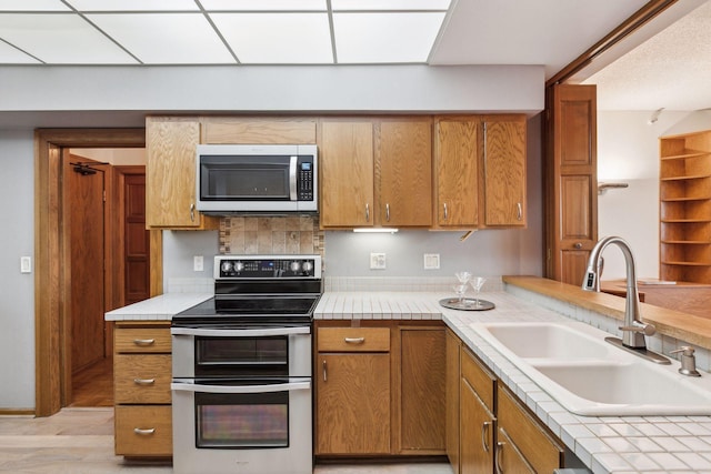 kitchen featuring light hardwood / wood-style floors, decorative backsplash, sink, stainless steel appliances, and tile countertops