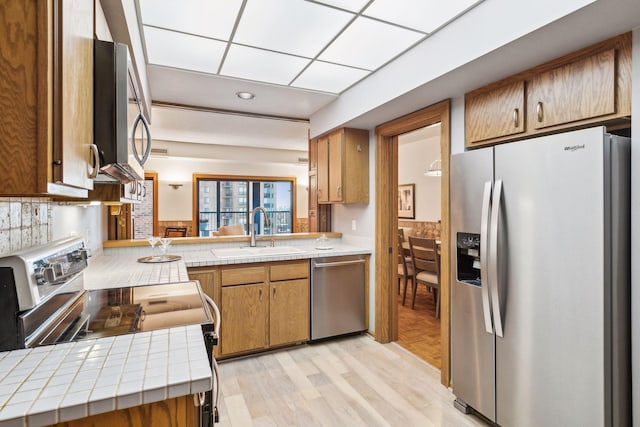 kitchen featuring kitchen peninsula, light hardwood / wood-style flooring, sink, stainless steel appliances, and tile counters