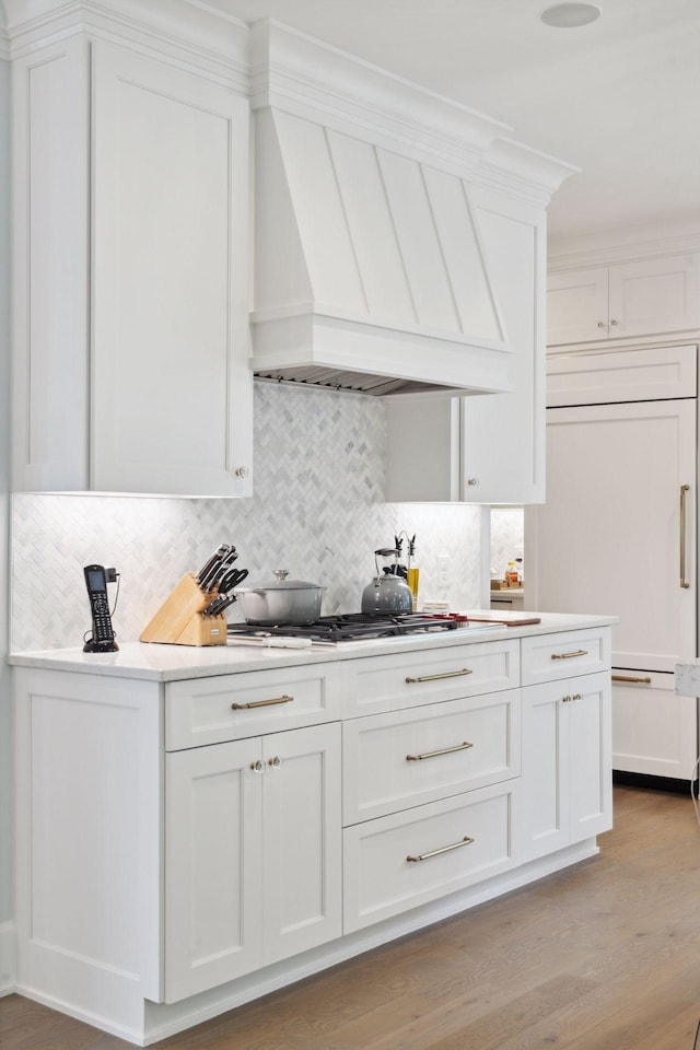 kitchen with decorative backsplash, white cabinets, light hardwood / wood-style flooring, and custom range hood