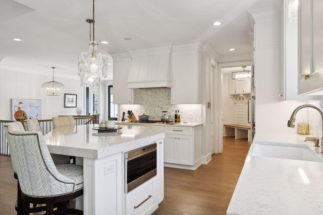 kitchen featuring white cabinets, appliances with stainless steel finishes, decorative light fixtures, sink, and custom range hood