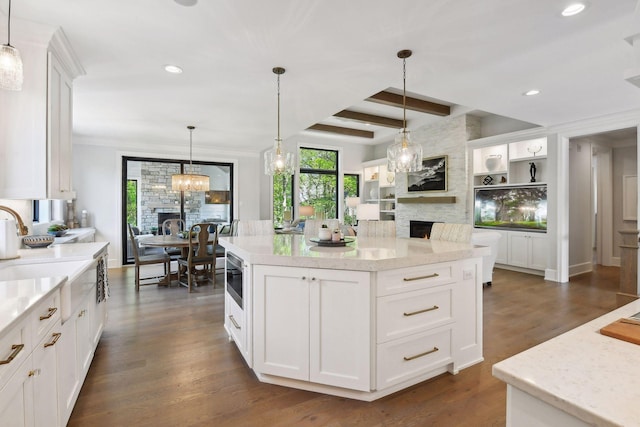 kitchen featuring white cabinets, pendant lighting, beam ceiling, and a stone fireplace