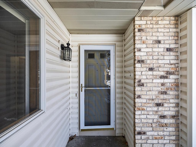 view of exterior entry featuring covered porch and brick siding