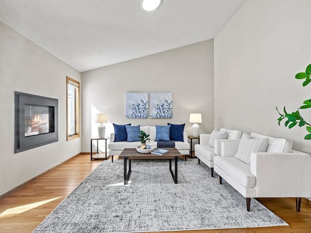 living room with a glass covered fireplace, lofted ceiling, a textured ceiling, and wood finished floors