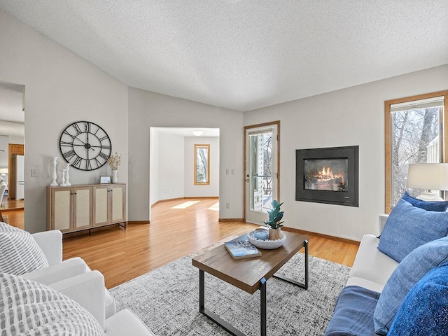 living area with baseboards, a textured ceiling, light wood-style flooring, and vaulted ceiling