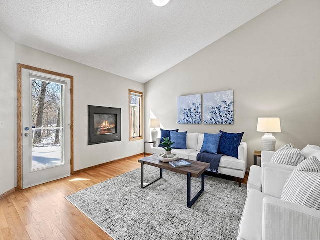 living area with a glass covered fireplace, lofted ceiling, light wood-type flooring, and a textured ceiling