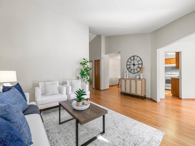 living area featuring light wood-type flooring, lofted ceiling, and baseboards