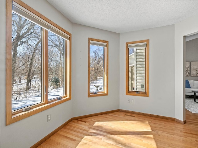 spare room featuring visible vents, baseboards, light wood finished floors, and a textured ceiling