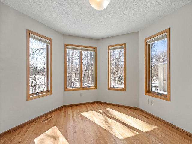 spare room featuring visible vents, a textured ceiling, baseboards, and wood finished floors