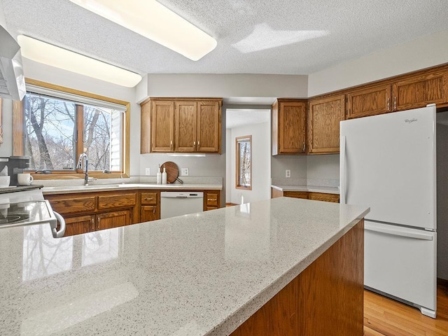 kitchen featuring white appliances, brown cabinetry, light wood-style flooring, a sink, and a textured ceiling