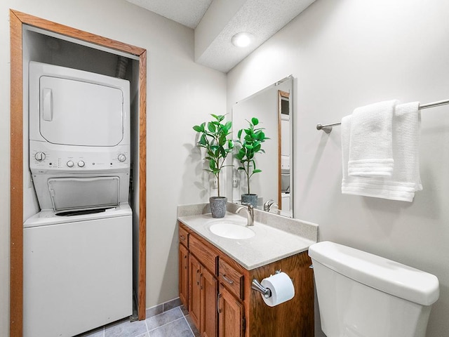 bathroom featuring tile patterned floors, toilet, vanity, and stacked washer / dryer