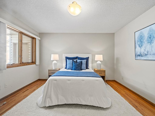 bedroom featuring a textured ceiling, baseboards, and wood finished floors