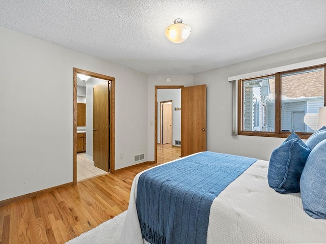 bedroom featuring light wood-style flooring, baseboards, visible vents, and a textured ceiling