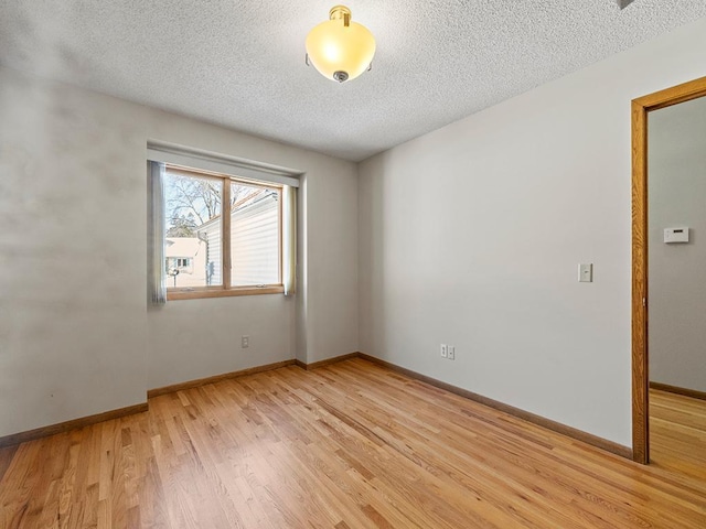 empty room featuring baseboards, light wood-style floors, and a textured ceiling