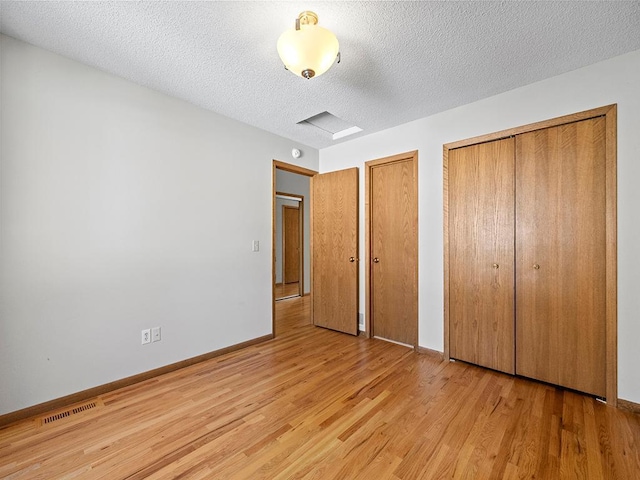 unfurnished bedroom with light wood-type flooring, visible vents, multiple closets, a textured ceiling, and baseboards