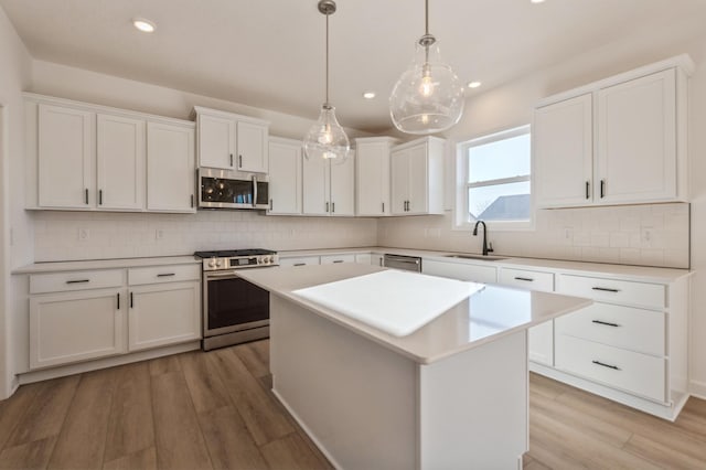 kitchen with appliances with stainless steel finishes, decorative light fixtures, sink, white cabinets, and a center island