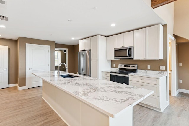 kitchen featuring white cabinets, stainless steel appliances, sink, light stone counters, and a center island with sink