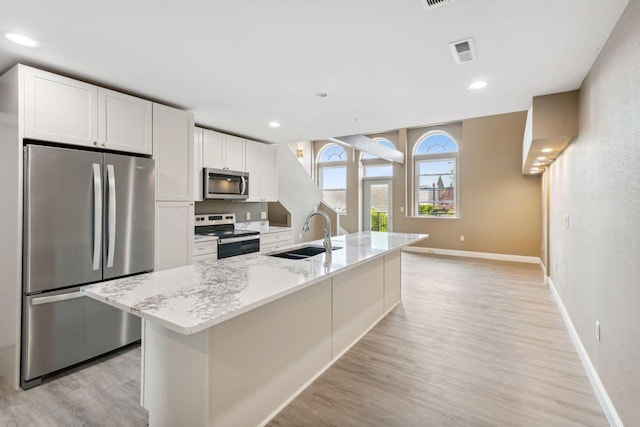 kitchen featuring appliances with stainless steel finishes, sink, white cabinetry, light stone countertops, and a center island with sink