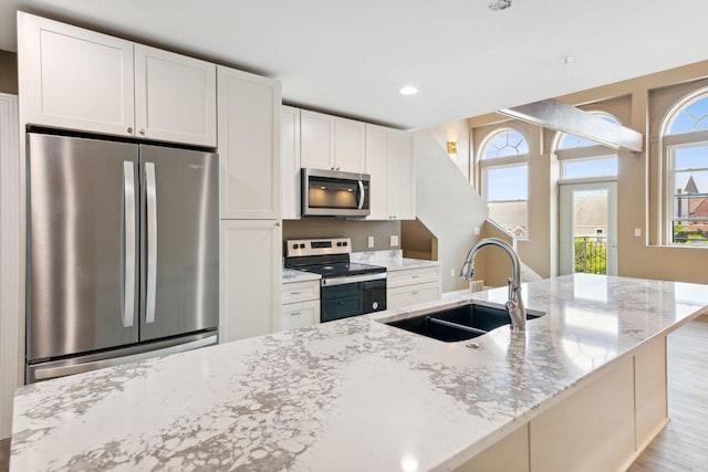 kitchen with sink, light stone counters, white cabinets, and stainless steel appliances