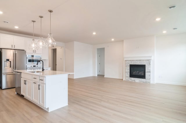 kitchen featuring white cabinets, stainless steel appliances, a kitchen island with sink, and decorative light fixtures