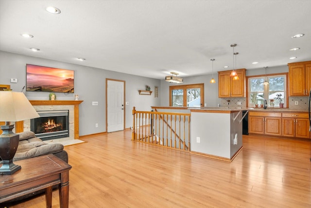 kitchen with a breakfast bar, decorative light fixtures, decorative backsplash, a tiled fireplace, and light hardwood / wood-style flooring