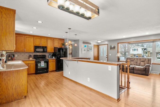 kitchen featuring sink, a kitchen bar, hanging light fixtures, black appliances, and light hardwood / wood-style flooring